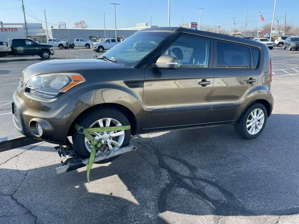 A Kia Soul strapped to a tow dolly in a parking lot mid-morning -- the loading step of a same-day junk car sale