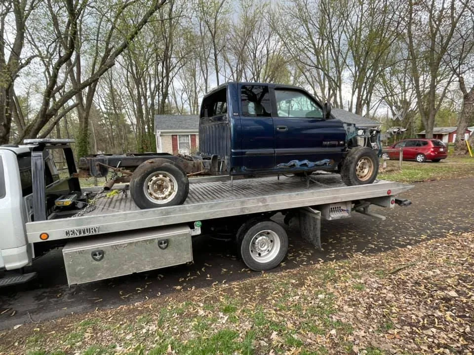 A stripped blue Dodge Ram secured on a flatbed tow truck -- even totaled trucks missing body panels hold parts value in Indianapolis