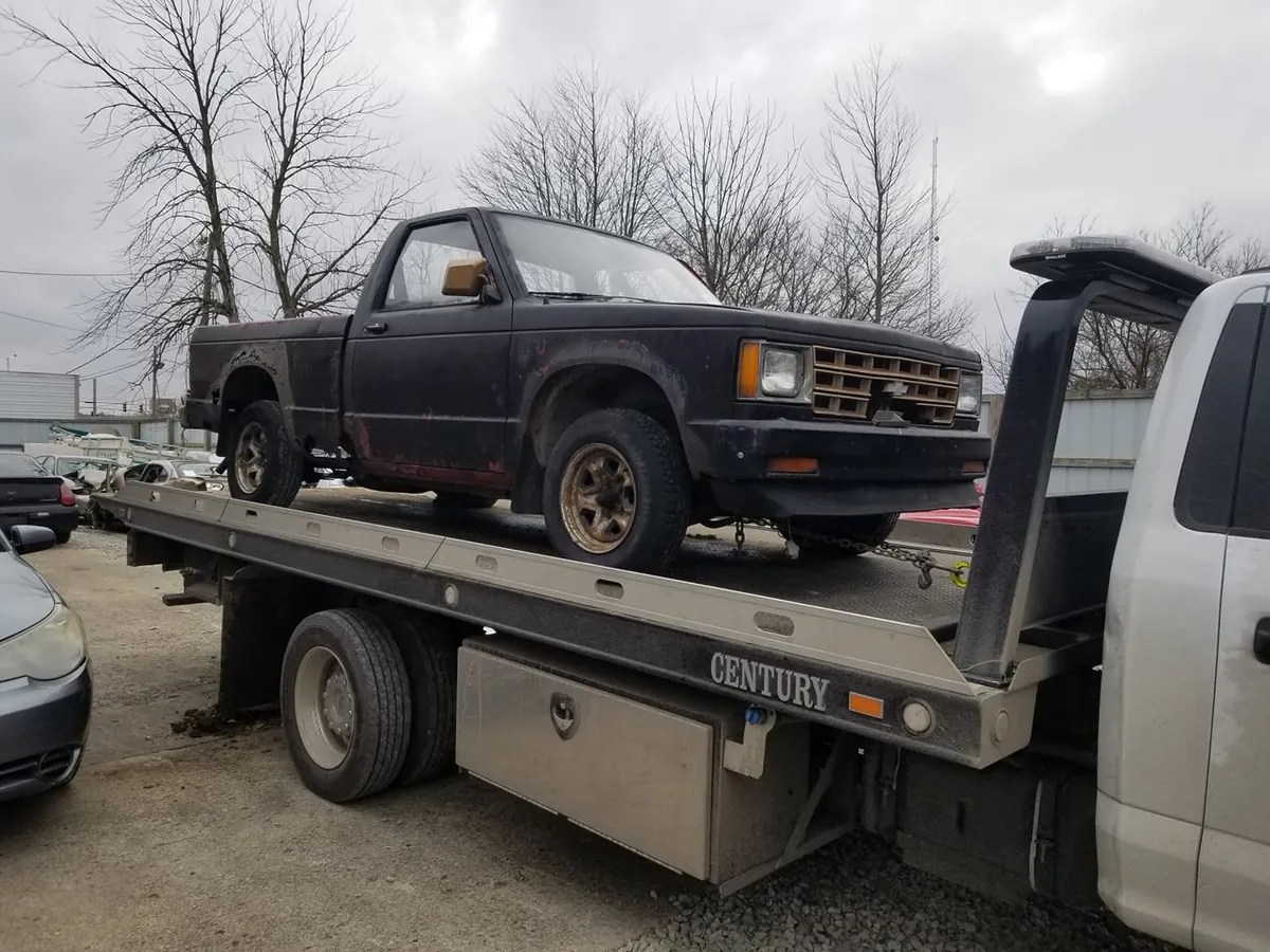 A rusted Chevy S10 winched onto a flatbed tow truck -- prep steps like clearing a path keep a pickup this smooth