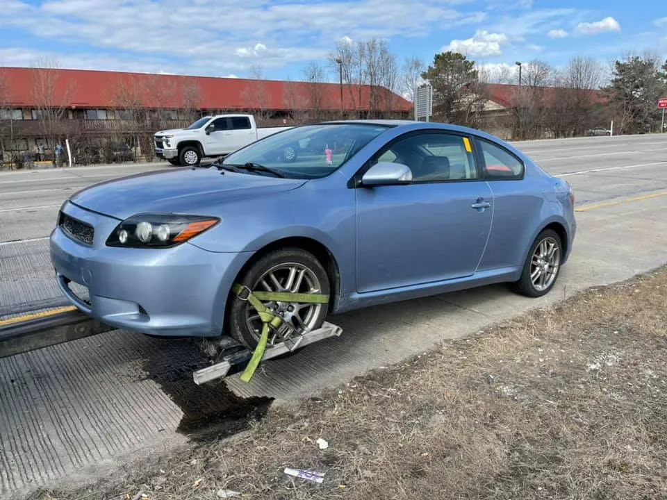 Non-running coupe being towed along an Indianapolis highway shoulder by a licensed junk car buyer