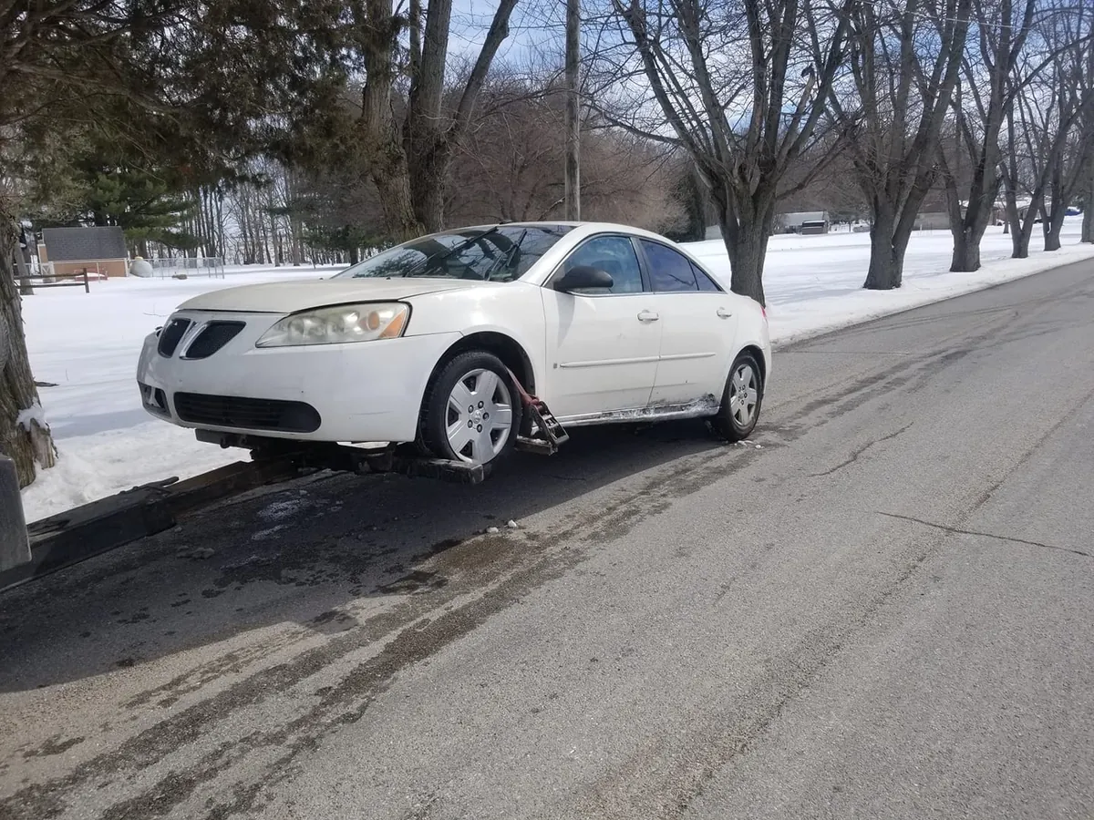 White Pontiac G6 that wouldn't start secured on a tow dolly on a snowy Indianapolis street -- non-running cars still sell for cash