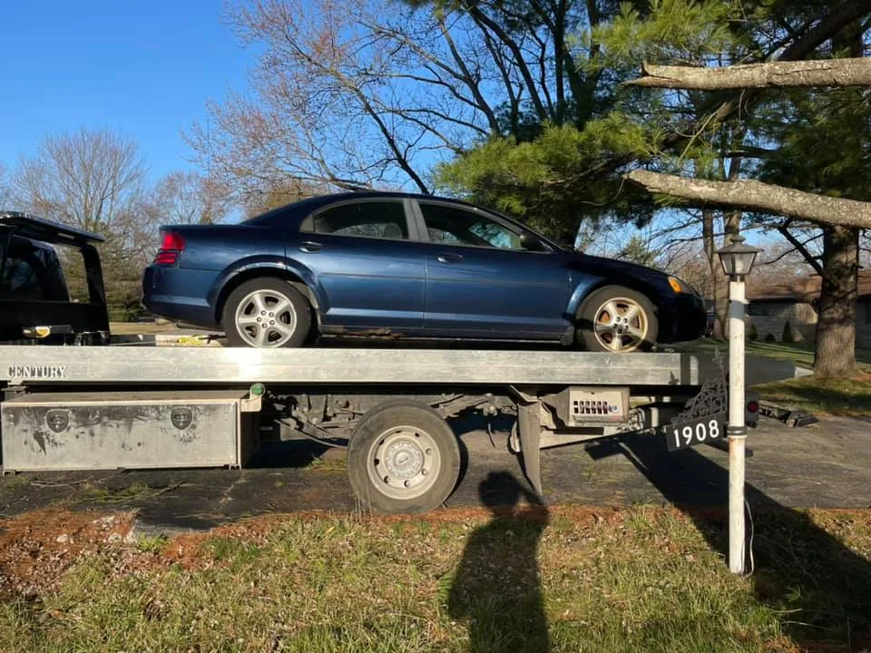 Blue sedan secured on a flatbed tow truck at an Indianapolis home, picked up while the seller's replacement title was still in the mail