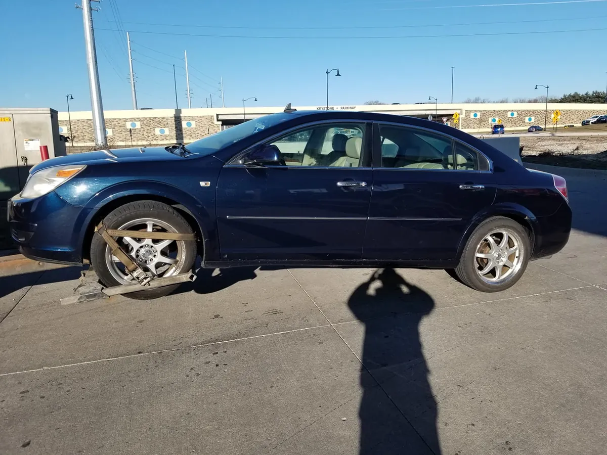 Dark blue Saturn Aura sedan strapped to a tow rig on a sunny Indianapolis day, waiting on its pre-sale checklist