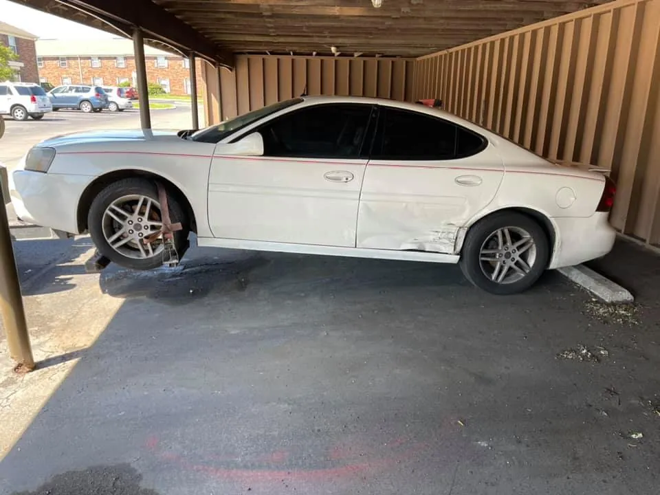 Damaged white Pontiac Grand Prix under an Indianapolis carport, waiting on junk car paperwork in Indiana before pickup