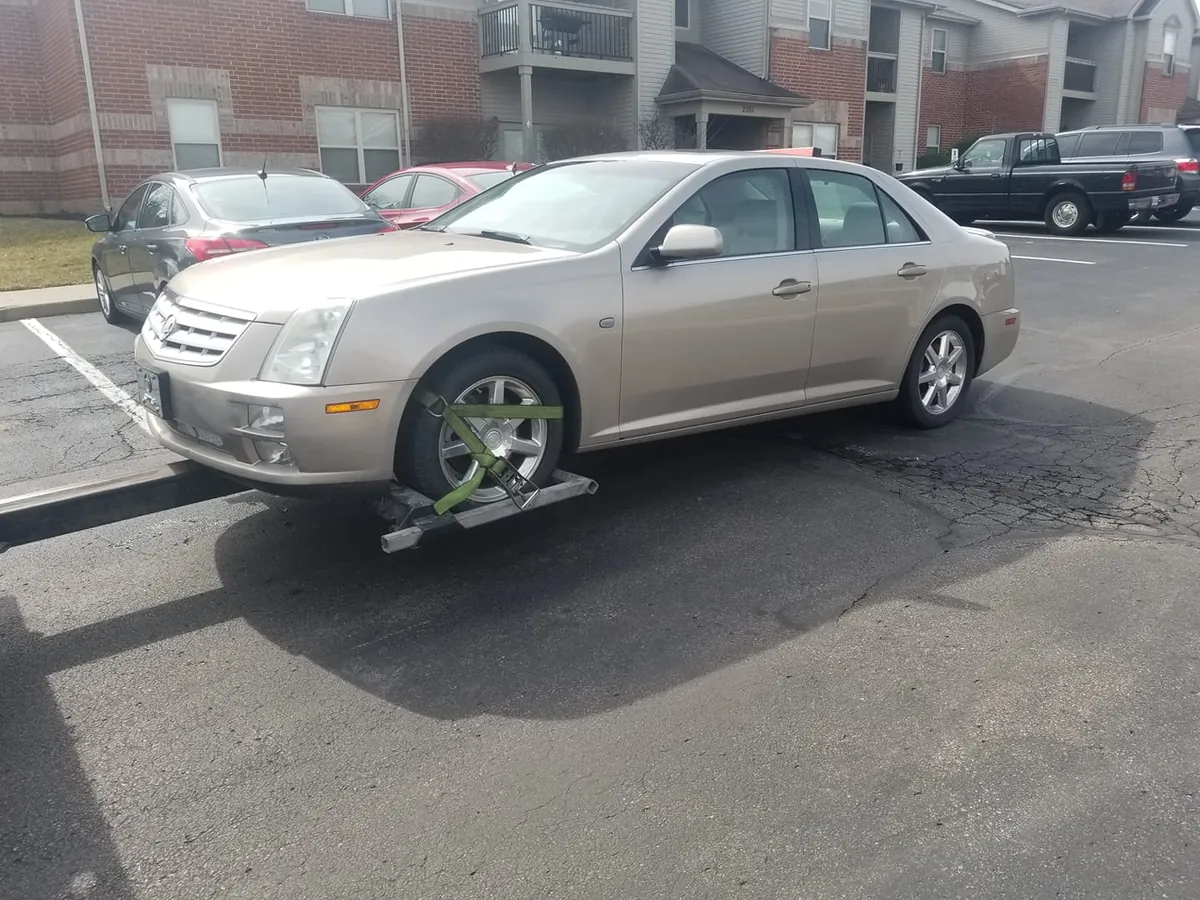 Tan Cadillac STS secured to a tow dolly outside an Indianapolis apartment complex, a complete unstripped car that holds its price tier