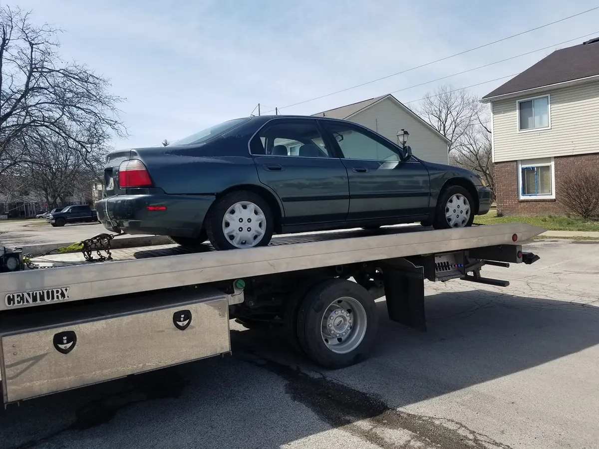 Dark green Honda Accord sedan loaded on a flatbed tow truck, a popular-parts vehicle in the $500 to $1,000 junk car tier