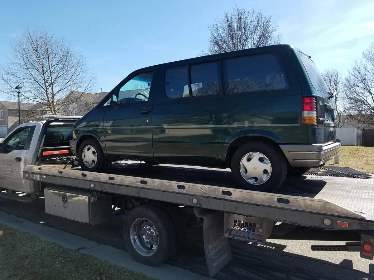 A flatbed driver loads a minivan on a residential street -- towing is always included in the offer, never billed