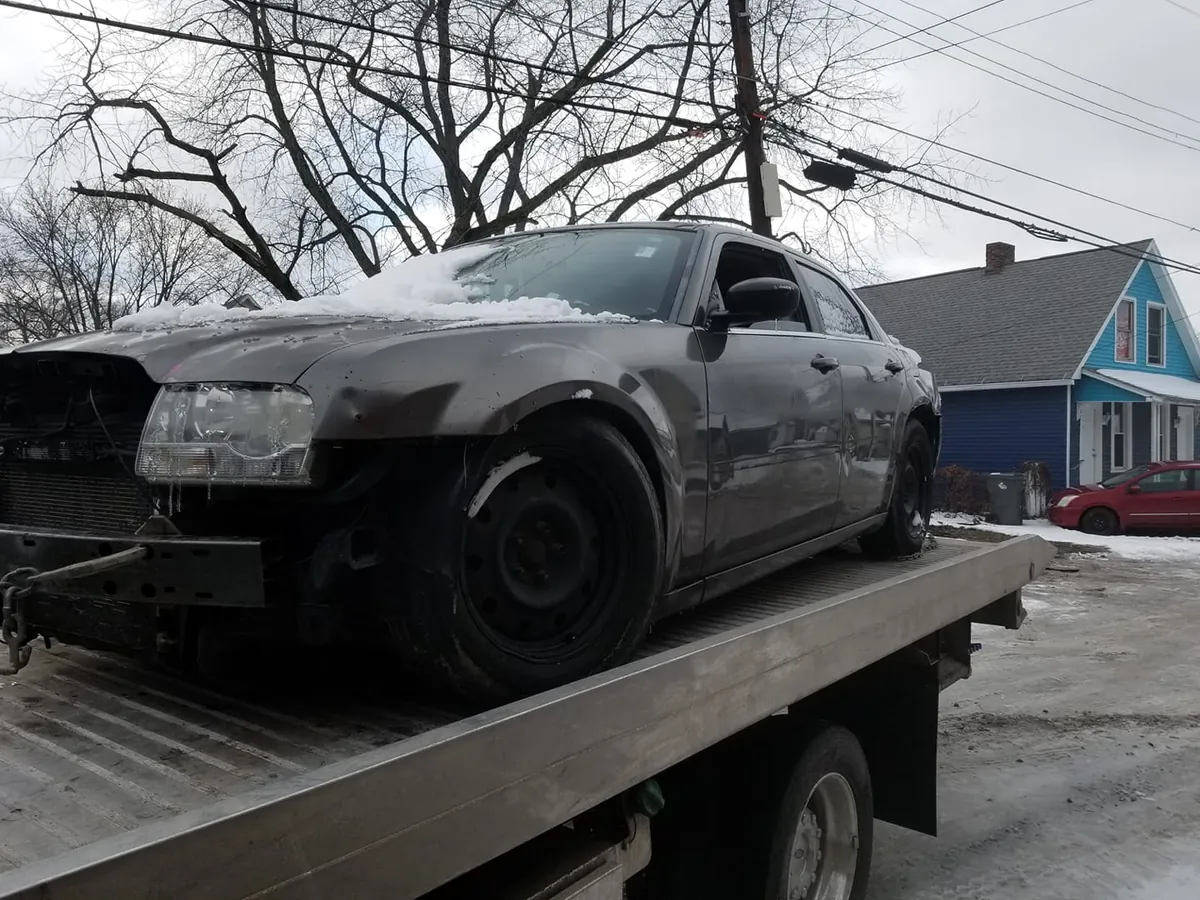 A gray Chrysler 300 with front-end damage on a flatbed in the snow -- totaled cars sell for cash in any season in Indiana