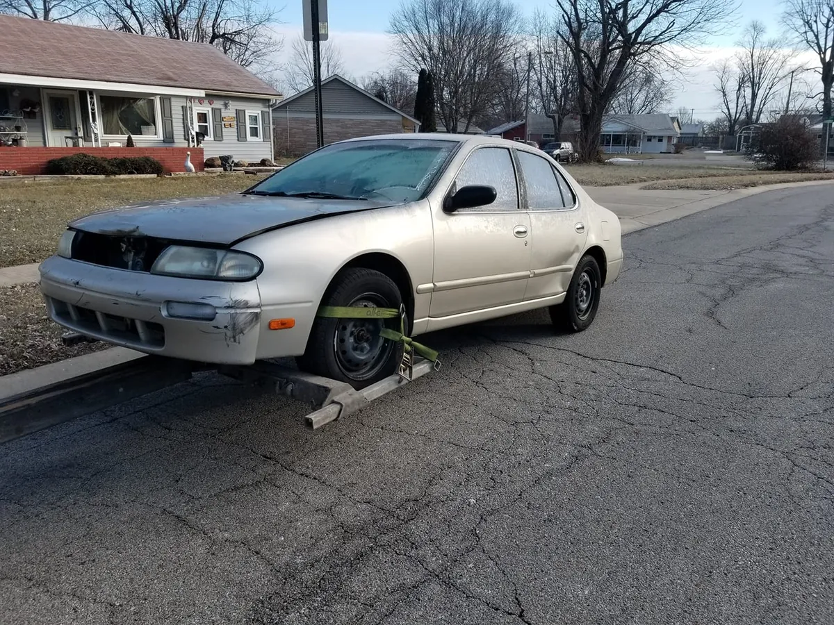 Gold Nissan Altima with front-end damage awaiting pickup, its engine and parts still worth more than its scrap weight